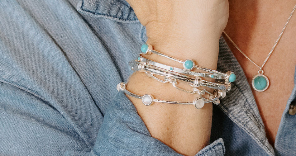 Person wearing silver hoop earrings, multiple bracelets, and a necklace with a blue background.1621243260e1af0c20-0